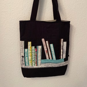 Könnte beinhalten: Schwarze Tragetasche mit Patchwork-Design aus bunten Stoffstreifen. Die Stoffstreifen sind so angeordnet, dass sie wie eine Reihe von Büchern aussehen. Der Text "STOE fabrics Memory Moos" und "DARLING collection" ist auf der Tasche sichtbar.