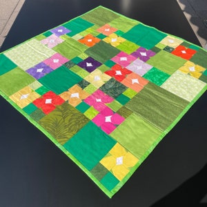 Könnte beinhalten: Eine grüne und weiße Steppdecke mit Patchwork-Muster, das bunte Blumen zeigt. Die Steppdecke besteht aus verschiedenen Stoffen mit unterschiedlichen Mustern und Texturen.