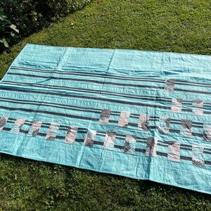 Könnte beinhalten: Eine türkisblaue Steppdecke mit schwarzen und weißen Streifen und einem geometrischen Muster. Die Steppdecke besteht aus zusammengenähten Stoffquadraten.