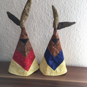 Könnte beinhalten: Zwei handgefertigte Stoffhasen-Ornamente. Einer ist gelb, rot und braun. Der andere ist gelb, blau und braun.