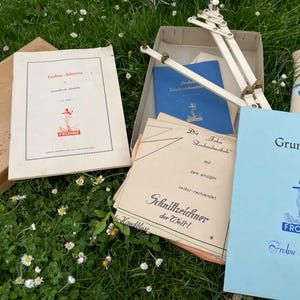 Könnte beinhalten: Ein Vintage-Nähmuster-Set mit einem blauen und weißen Heftchen mit dem Titel "Grundbuch Frohne Modelle" und einem weißen Nähwerkzeug aus Kunststoff. Das Set enthält ein Heftchen mit dem Titel "Frohne Schnitte" und ein Heftchen mit dem Titel "Die Frohne Schnittzeichenmethode mit dem einzigen selbst-rechnenden Schnittzeichner der Welt!"