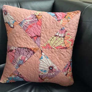 Könnte beinhalten: Ein rosa-weißes Dekokissen mit gestepptem Muster. Das Kissen ist aus Stoff mit Blumenmuster und mit einem geometrischen Muster verziert.