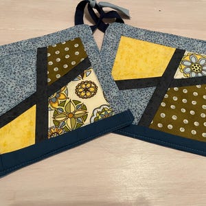 Könnte beinhalten: Zwei blaue und marineblaue gequiltete Topflappen mit geometrischen Mustern in Gelb, Grün, Braun und Weiß.