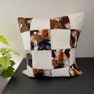 Könnte beinhalten: Ein weißes Kissen mit Patchwork-Muster, das braune, weiße und schwarze Pferde zeigt. Das Kissen ist gesteppt mit einem erhabenen Muster.