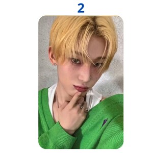 Op de afbeelding: Een fotokaart met een persoon met lichtblond haar en een groene trui. De persoon draagt een wit ondershirt en ringen. Het nummer "2" staat in een blauw vak bovenaan in het midden van de kaart.