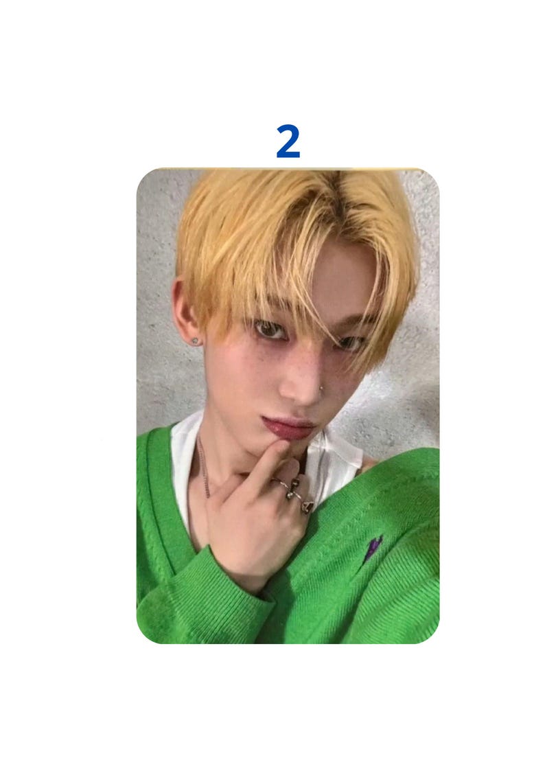 Op de afbeelding: Een fotokaart met een persoon met lichtblond haar en een groene trui. De persoon draagt een wit ondershirt en ringen. Het nummer "2" staat in een blauw vak bovenaan in het midden van de kaart.