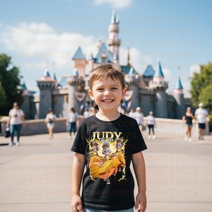 May include: A black t-shirt featuring a graphic of three cartoon characters with the text "Judy Hopps". The characters are set against a yellow and gold lightning bolt design. The background shows a castle and people.