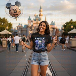 May include: A woman in a black t-shirt with the text "PAWBERT Lynxley" and a cartoon graphic, holding a Mickey Mouse balloon and an ice cream. A castle is in the background.