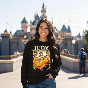 May include: Black sweatshirt featuring a graphic of Judy Hopps from Zootopia, with the text "JUDY Hopps" in gold. The design includes Judy in a yellow dress with lightning bolt accents. The background shows a castle.