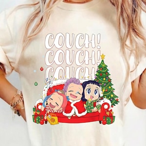 May include: Cream-colored t-shirt featuring a cartoon illustration of three anime-style characters on a red couch with a Christmas tree. The text "COUCH!" is stacked above the characters. Presents and ornaments are also visible.