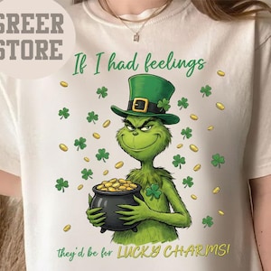 May include: Cream-colored t-shirt featuring a green cartoon character wearing a green hat and holding a pot of gold. The text reads "If I had feelings they'd be for LUCKY CHARMS!" with shamrocks and gold coins.