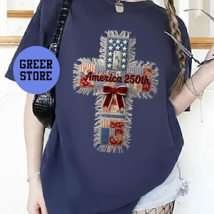 以下が含まれることがあります： 赤、白、青のパッチワーク模様の十字架のデザインが特徴のネイビーブルーのTシャツ。「America 250th」の文字と赤いリボンが付いています。左側には「Greer Store」と書かれた青い円があります。