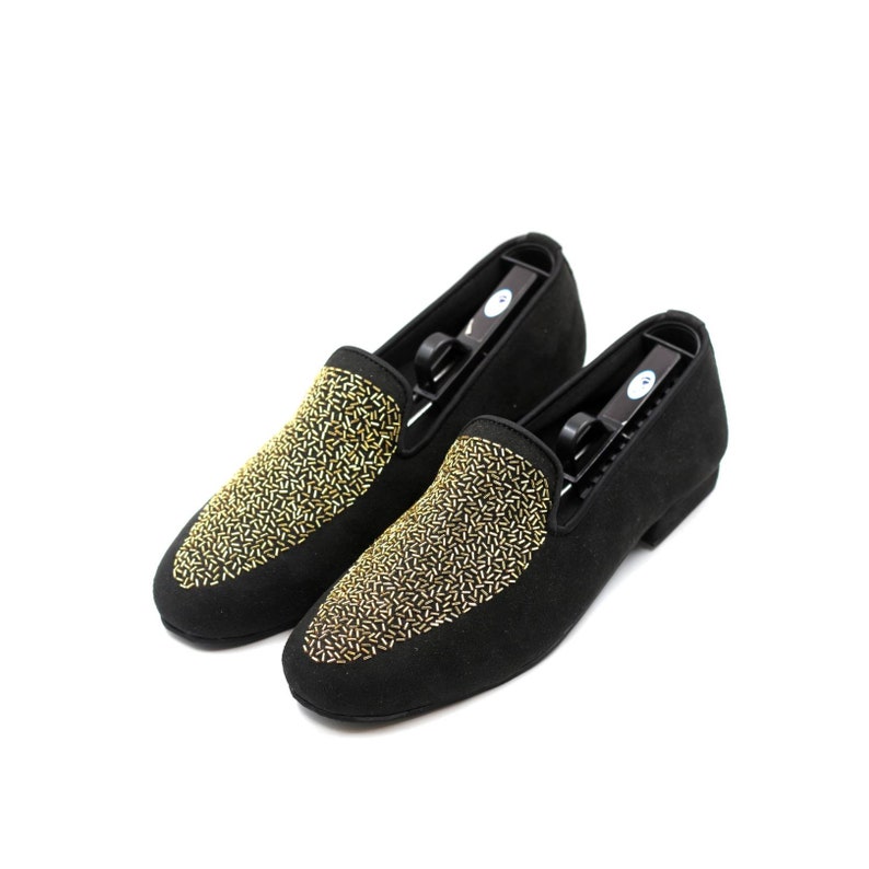 May include: A pair of black suede loafers with gold embroidered detailing. The loafers have a rounded toe and a low heel.