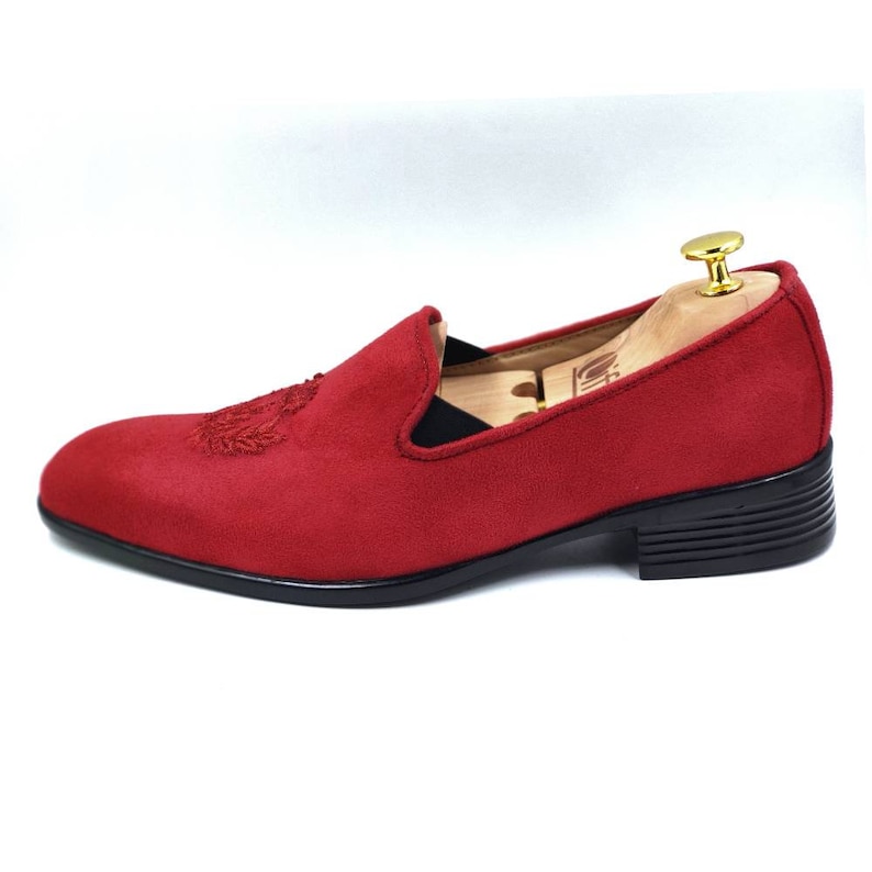 May include: Red suede loafers with a black heel and a decorative embroidered design on the toe.