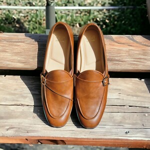 May include: A pair of brown leather loafers with a buckle strap. The loafers have a pointed toe and a low heel.
