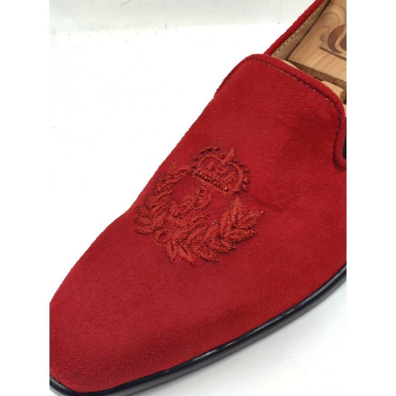 May include: Red suede loafers with an embroidered crown and laurel wreath design.