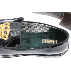 Pu&ograve; includere: Mocassino in pelle verniciata nera con un ornamento a corona dorata. La scarpa &egrave; foderata in velluto verde e ha un sottopiede con motivo argento e nero. Il nome del marchio "HSHH" &egrave; stampato sul sottopiede.