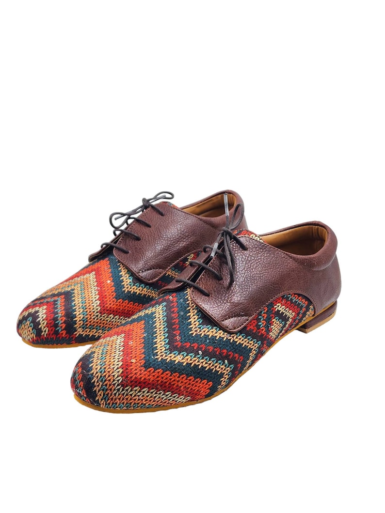 Puede incluir: Un par de zapatos marrones de cuero con cordones y un patr&oacute;n geom&eacute;trico colorido en la punta.
