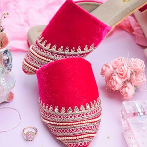 May include: A pair of pink velvet slippers with gold and silver embroidery and pearl accents. The slippers have a pointed toe and a low heel.