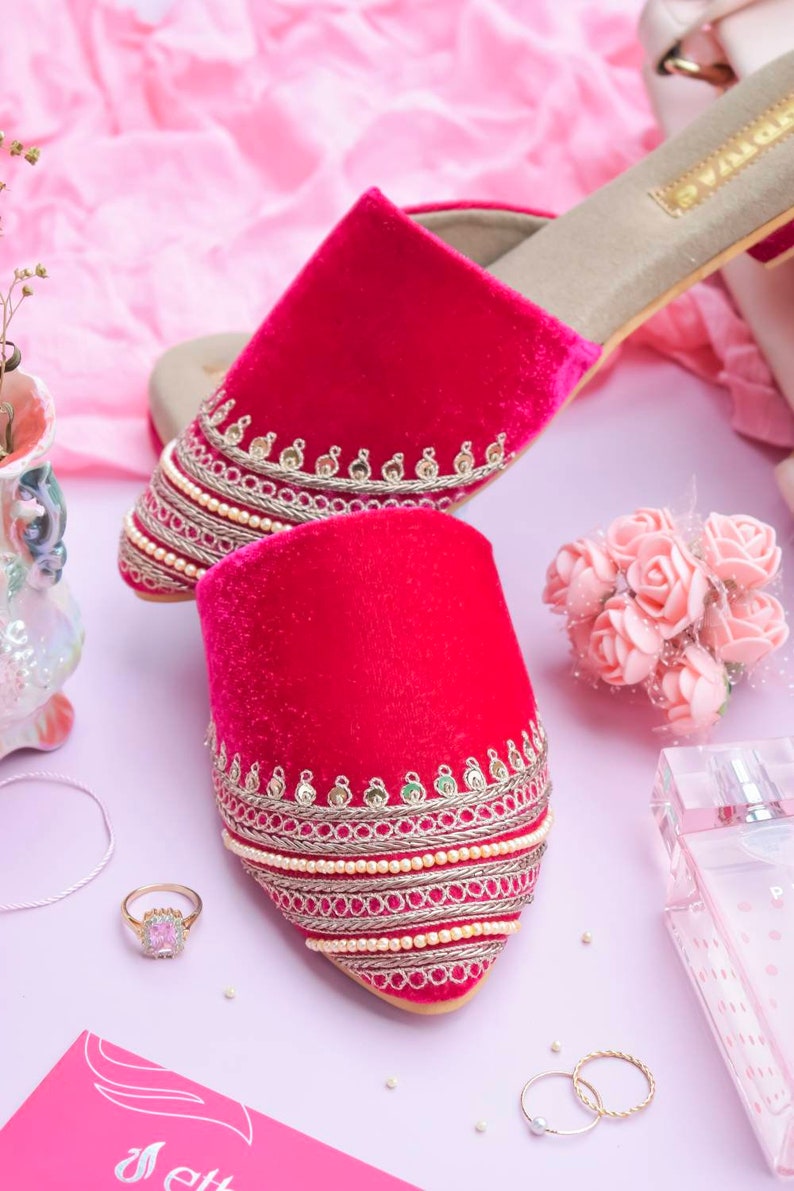 May include: A pair of pink velvet slippers with gold and silver embroidery and pearl accents. The slippers have a pointed toe and a low heel.