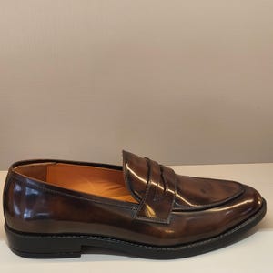 Pu&ograve; includere: Mocassino in pelle marrone con finitura lucida. La scarpa presenta una punta arrotondata, una fascia sul collo del piede e una suola nera. L'interno &egrave; di colore marrone chiaro. Misura circa 28 cm di lunghezza.