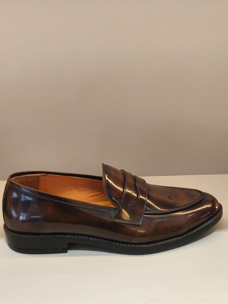 Pu&ograve; includere: Mocassino in pelle marrone con finitura lucida. La scarpa presenta una punta arrotondata, una fascia sul collo del piede e una suola nera. L'interno &egrave; di colore marrone chiaro. Misura circa 28 cm di lunghezza.