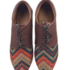 Puede incluir: Un par de zapatos de cuero marr&oacute;n con un patr&oacute;n geom&eacute;trico colorido en la punta. Los zapatos tienen cordones y una punta redondeada.