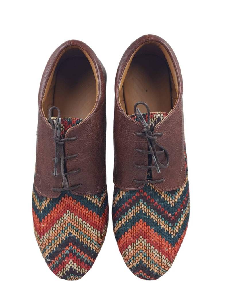 Puede incluir: Un par de zapatos de cuero marr&oacute;n con un patr&oacute;n geom&eacute;trico colorido en la punta. Los zapatos tienen cordones y una punta redondeada.