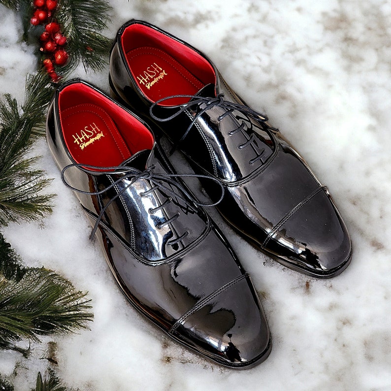 May include: Two black patent leather lace-up shoes with red lining and gold lettering that reads "Hash Handmade".