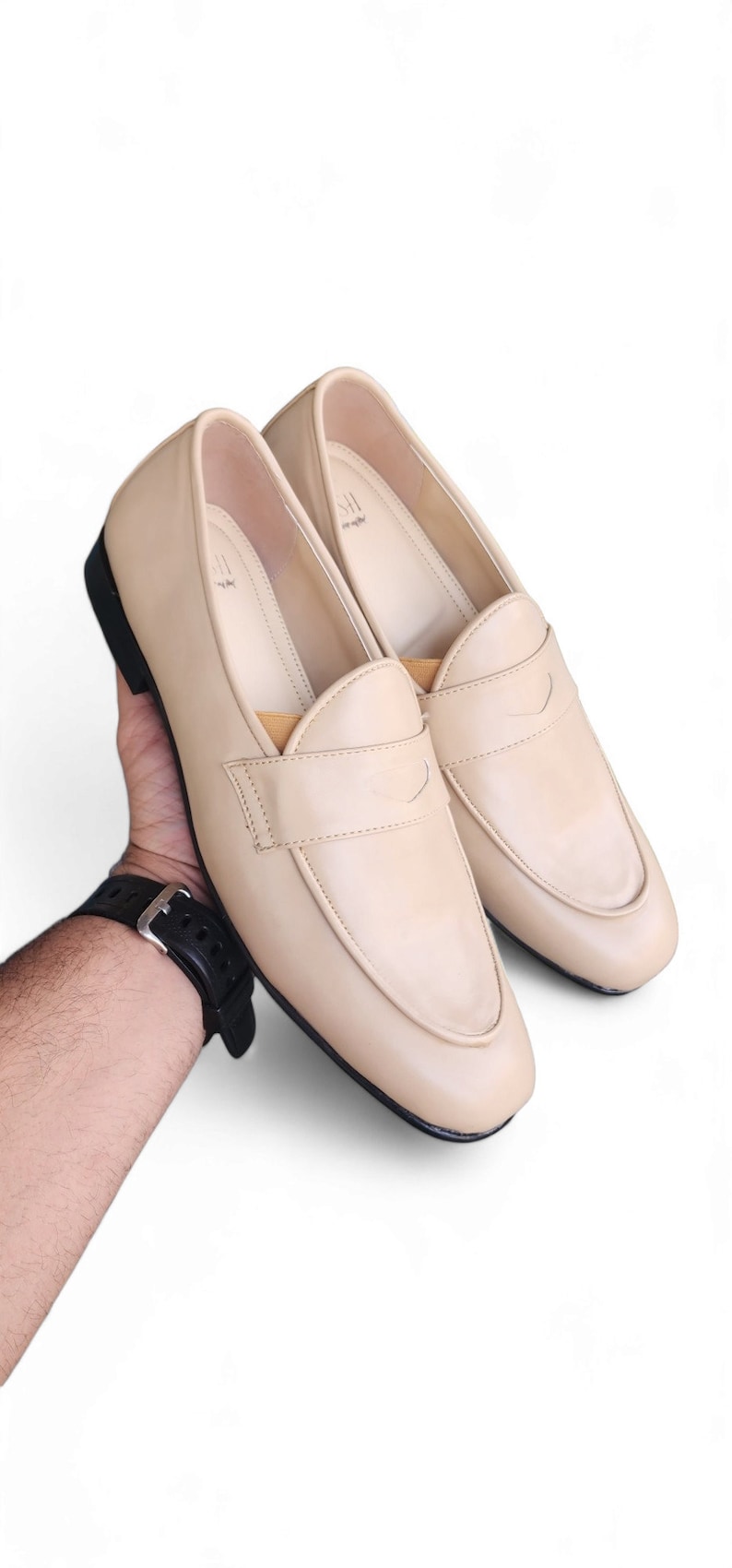 May include: A pair of beige leather loafers with a black sole. The loafers have a simple design with a single strap across the top.