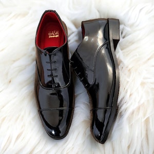 May include: A pair of black leather dress shoes with a cap toe and lace-up closure. The shoes have a shiny finish and the brand name "HASH" is visible on the inside of the shoe.