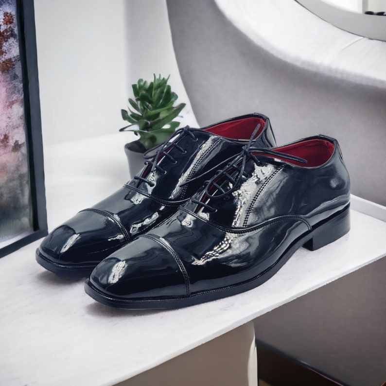 May include: A pair of black leather lace-up shoes with a cap toe design. The shoes have a glossy finish and red lining.