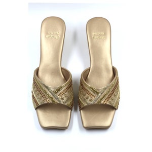 May include: A pair of gold heeled sandals with a square toe and intricate beaded embroidery. The sandals are labeled "SHRIYA CRAFTS".