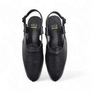 May include: A pair of black leather slip-on shoes with a slingback strap. The shoes have a pointed toe and the brand name "HASH" is printed on the insole.