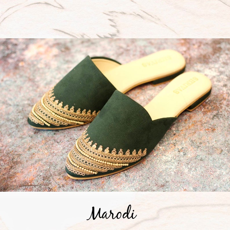 May include: A pair of dark green suede slippers with gold embroidery and a pointed toe. The slippers have a flat sole and are made by the brand "Marodi".