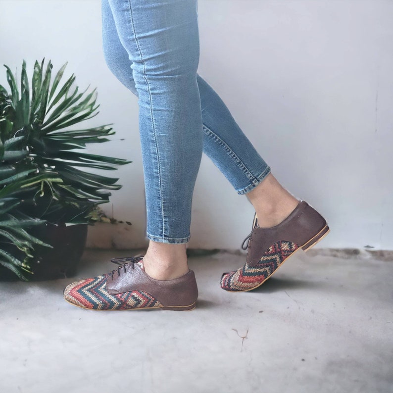 Puede incluir: Un par de zapatos de cuero marr&oacute;n con un patr&oacute;n tejido colorido en la punta y el tal&oacute;n. Los zapatos son usados por una persona que lleva jeans azules.