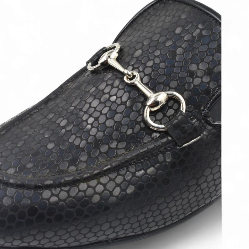 Puede incluir: Zapatos de vestir negros de cuero con estampado de piel de serpiente y detalle de bocado de caballo plateado.