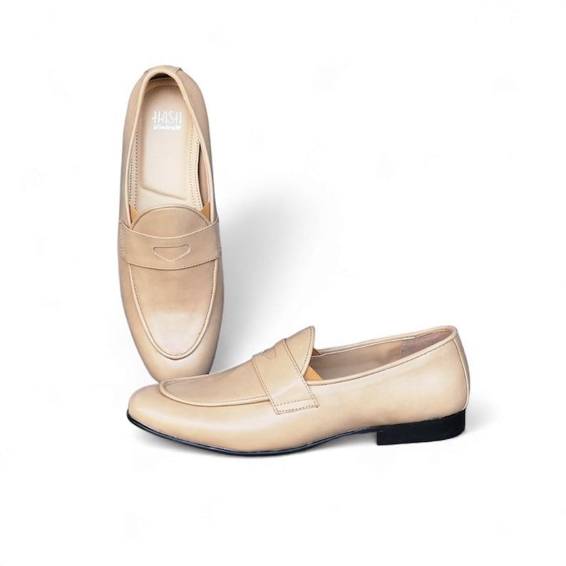 May include: A pair of beige leather loafers with a simple design. The loafers have a rounded toe and a slip-on style.