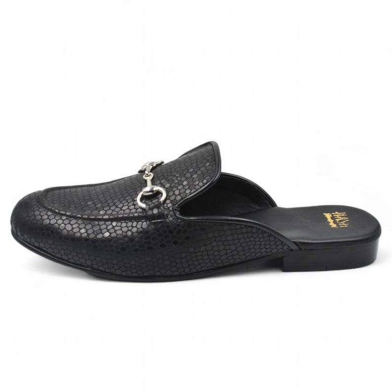Puede incluir: Mule de cuero negro con estampado de piel de serpiente y hebilla de metal plateado. El zapato tiene un tac&oacute;n peque&ntilde;o y una punta puntiaguda.