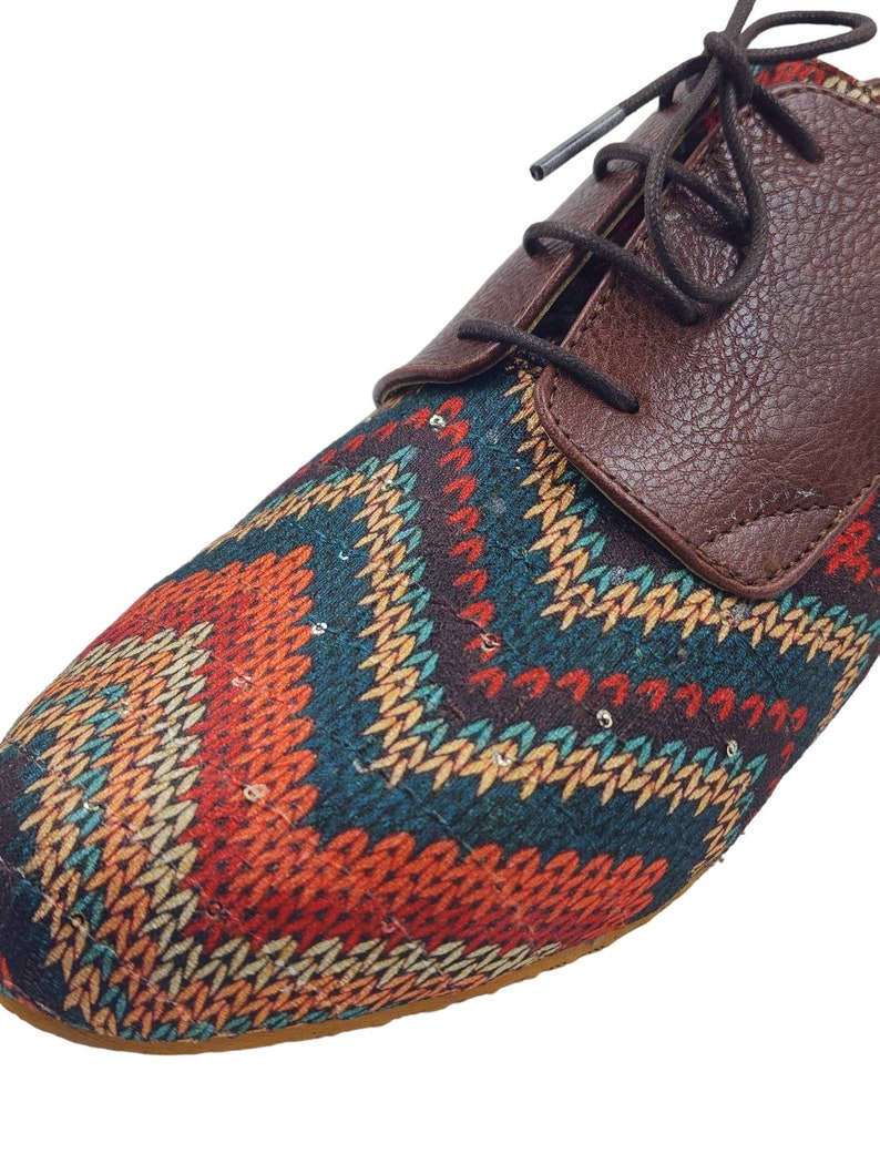 Puede incluir: Zapatos marrones de cuero con cordones y una puntera de tela con estampado geom&eacute;trico de colores.