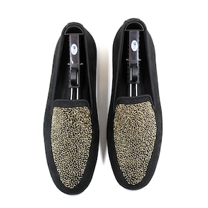 May include: A pair of black suede loafers with gold embellishments. The loafers have a pointed toe and a slip-on design.
