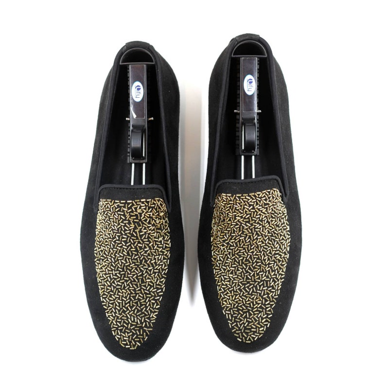 May include: A pair of black suede loafers with gold embellishments. The loafers have a pointed toe and a slip-on design.