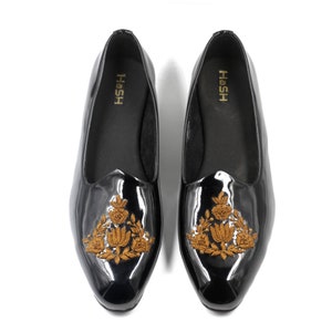 May include: A pair of black leather slip-on shoes with gold embroidery. The shoes have a pointed toe and a low heel. The embroidery features a floral design.