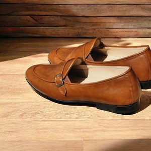 May include: Two brown leather shoes with a buckle strap. The shoes have a pointed toe and a low heel.