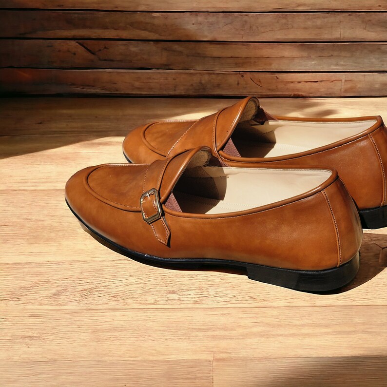 May include: Two brown leather shoes with a buckle strap. The shoes have a pointed toe and a low heel.