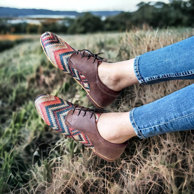 Puede incluir: Un par de zapatos de cuero marr&oacute;n con empeines de tela estampada de colores. Los zapatos tienen cordones y los lleva una persona que lleva pantalones vaqueros azules.