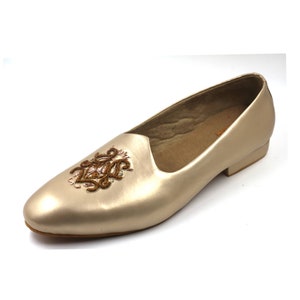 May include: Gold leather flat shoes with a brown embroidered design on the toe.
