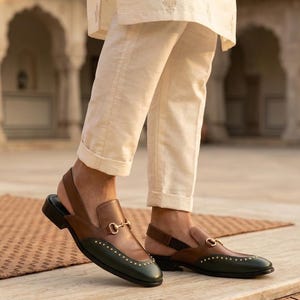 Puede incluir: Mocasines slingback de cuero marrón y verde, con detalles metálicos dorados. Los zapatos tienen una parte superior marrón y una puntera verde adornada con pequeños tachuelas doradas. La correa trasera también es marrón.