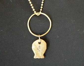 Könnte beinhalten: Eine goldene Kettenkette mit einem großen, runden Anhänger und einem kleineren, unregelmäßig geformten Anhänger. Die Kette wird von einer Person mit dunklen Haaren getragen.