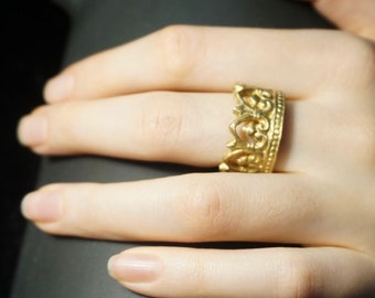 May include: A gold crown ring with intricate details. The ring is worn on a person's finger.